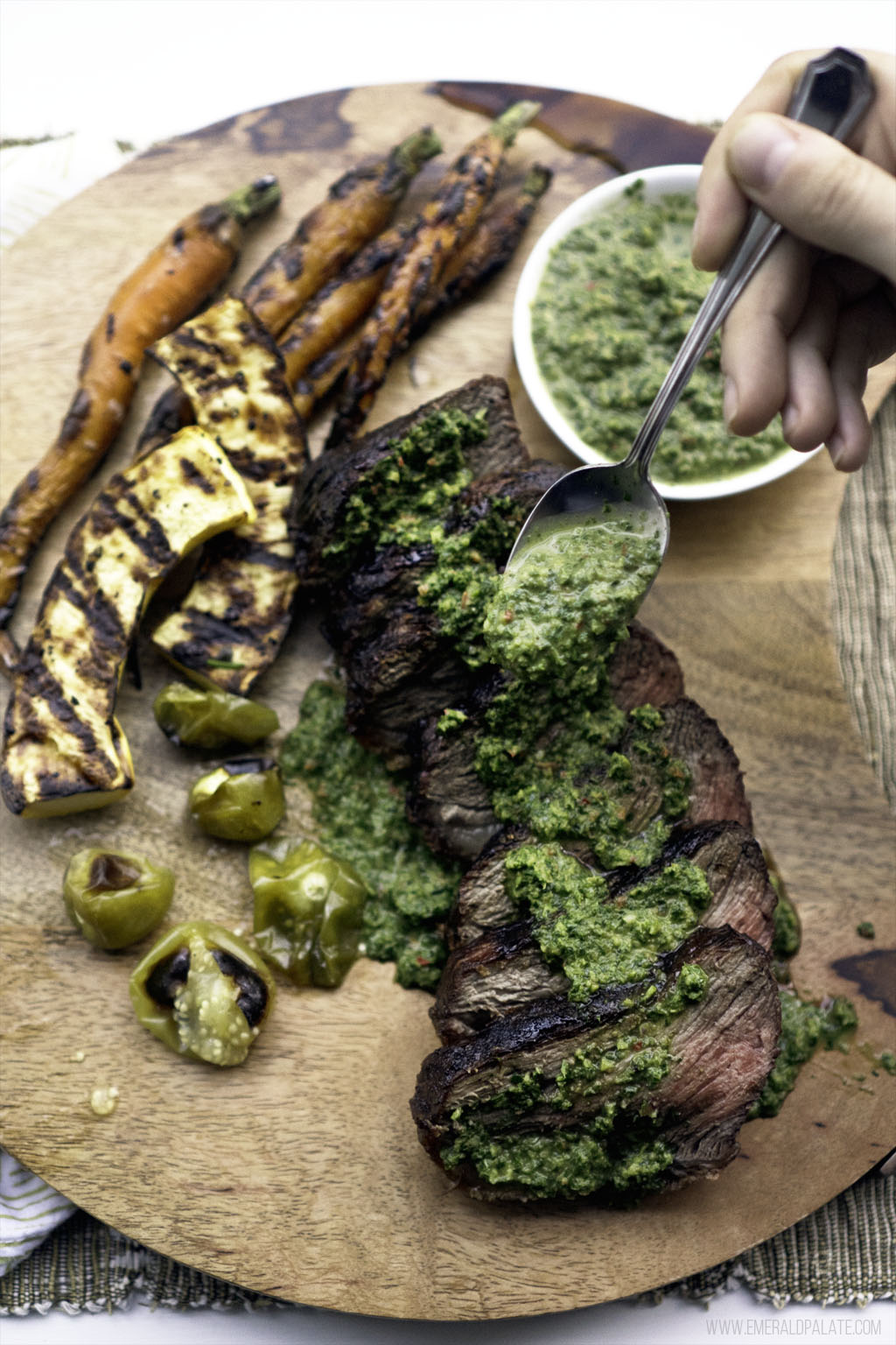 person drizzling carrot top chimichurri over grilled steak