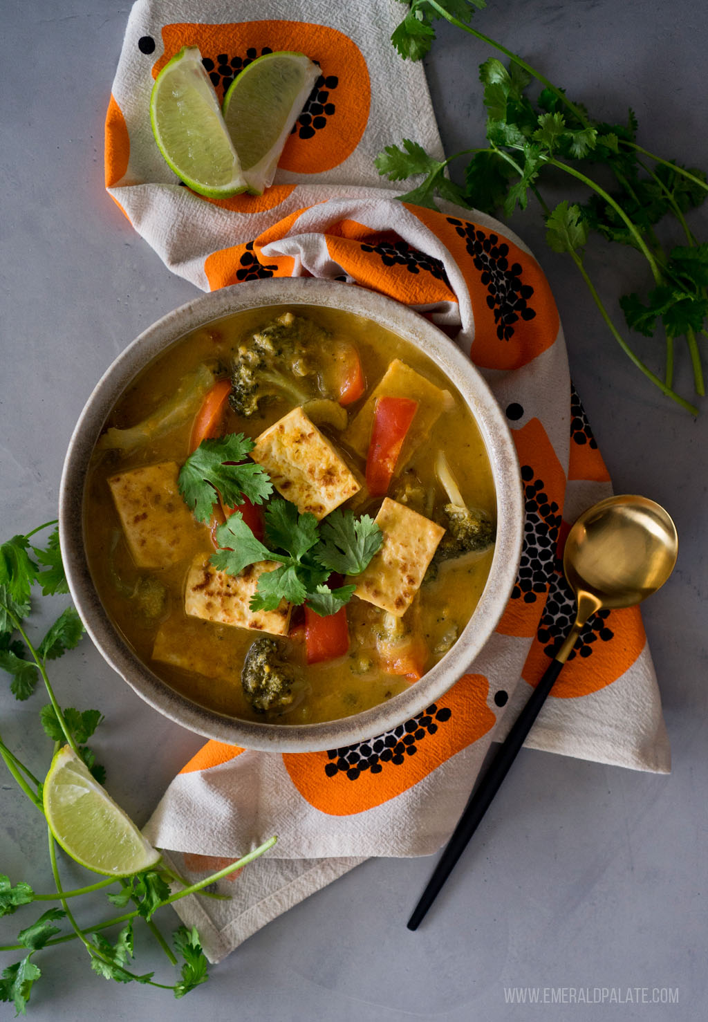 overhead shot of homemade pumpkin curry with tofu on a table with a napkin, spoon, cilantro, and lime