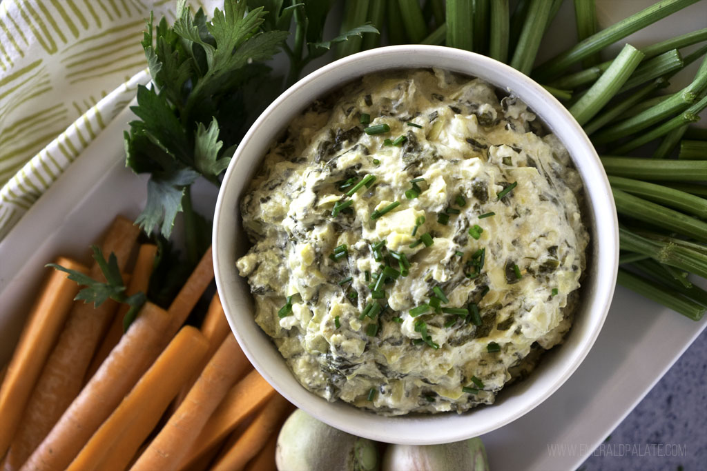 Dip made with celery root, artichoke, and spinach on a platter with vegetables