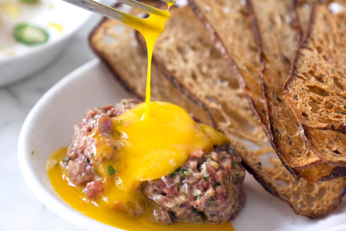 Person breaking the egg on one of the best steak tartare in Seattle