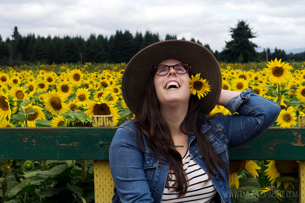 woman laughing at a sunflower farm with sunflower behind her ear