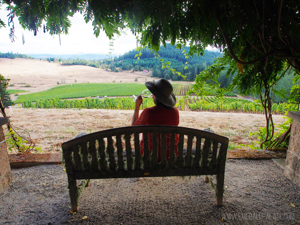 woman drinking on a bench overlooking vineyards at one of the best wineries in Willamette Valley