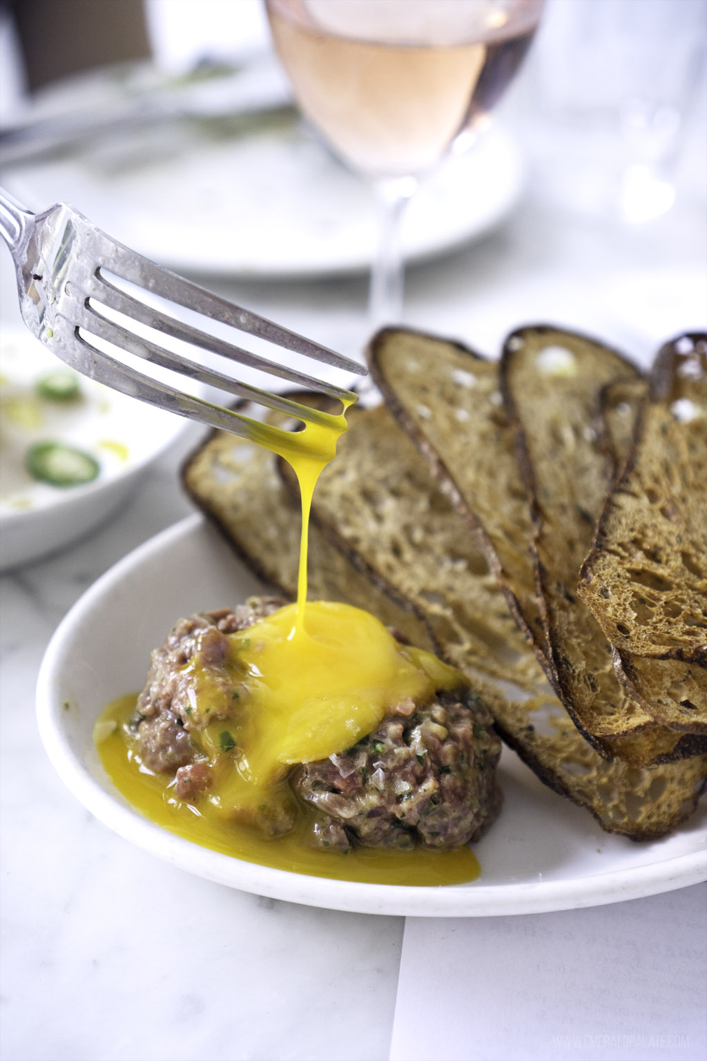 egg yolk dripping off a fork onto steak tartare