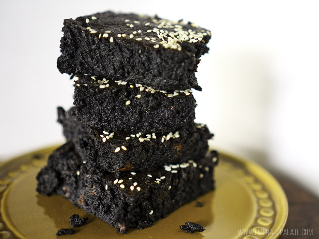 4 moist coconut banana fudge brownies stacked on a plate with coconut oil and sesame seeds