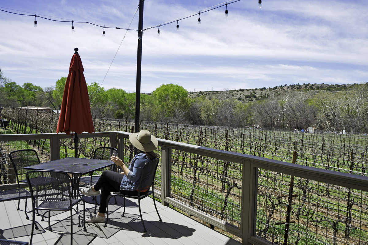 woman sitting on a patio overlooking vineyards at one of the best Cottonwood wineries in Arizona