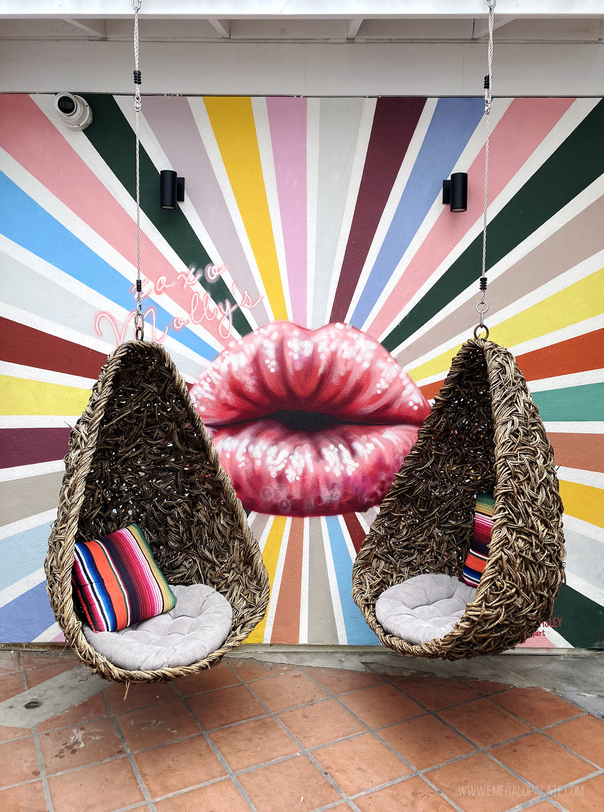 swinging pod chairs in front of a colorful mural with lips puckered in a kiss