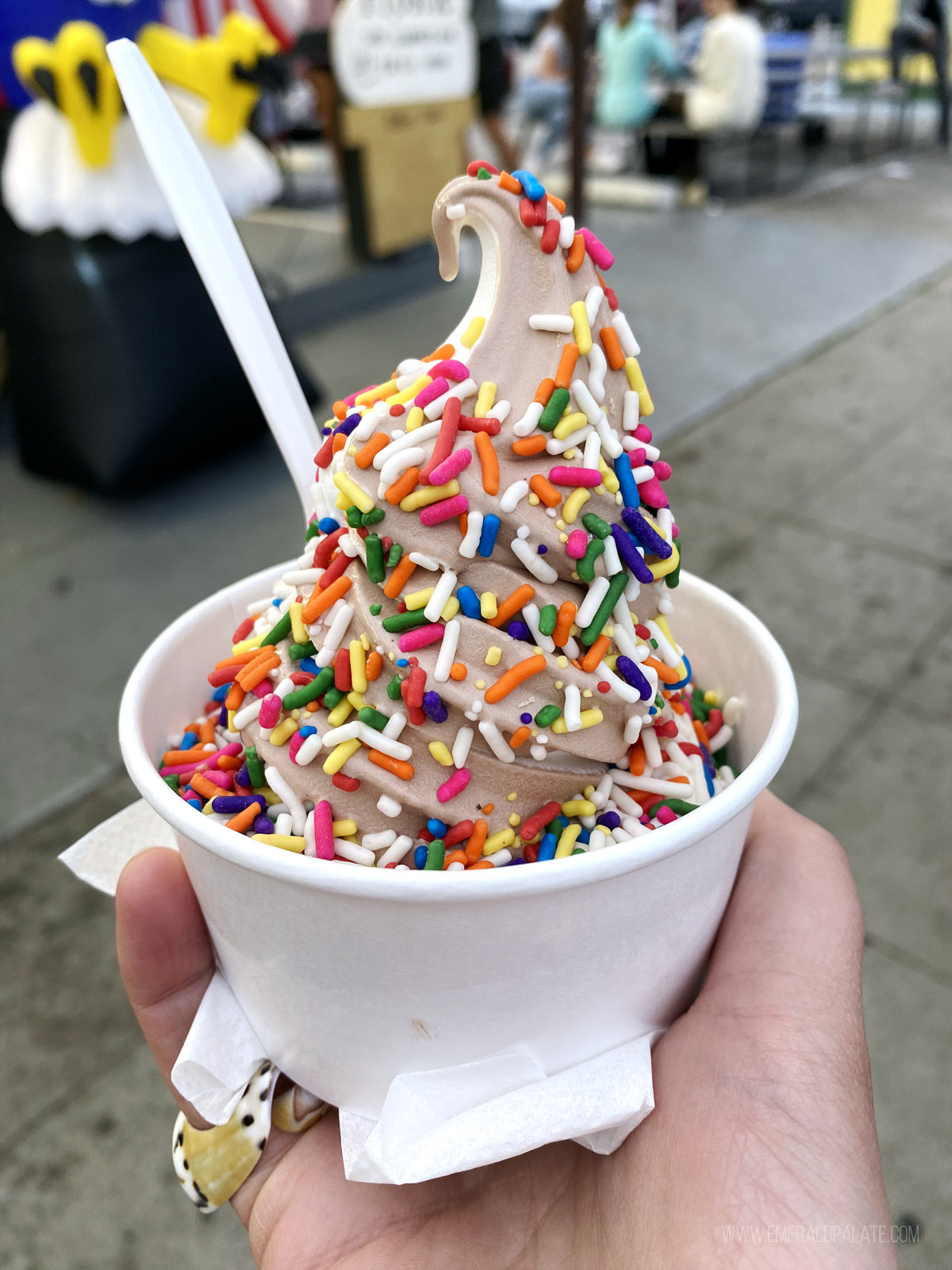 person holding a cup of soft serve ice cream with rainbow sprinkles
