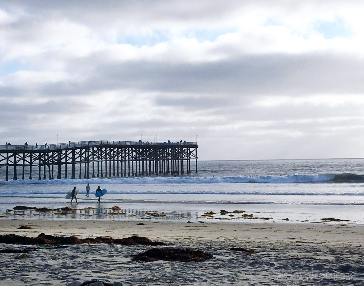 surfers walking into the ocean by a pier on Pacific Beach in San Diego