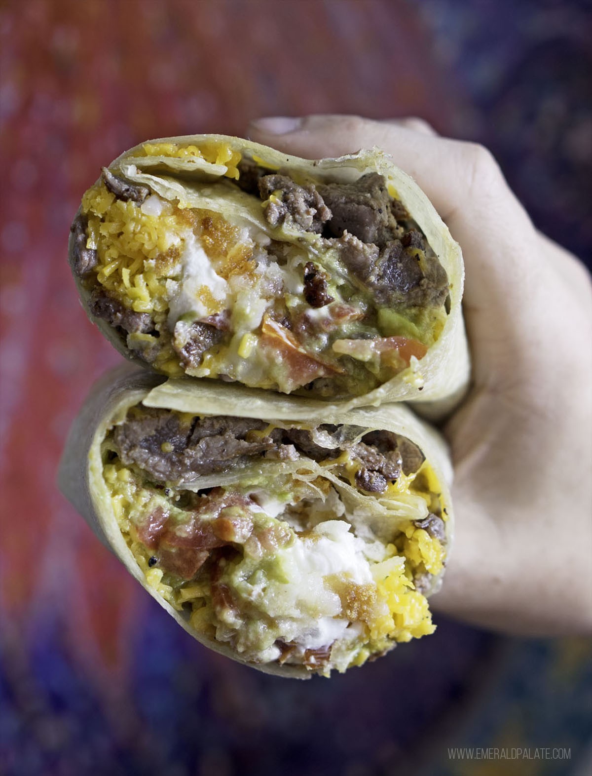 person holding two halves of a California burrito stacked on top of each other