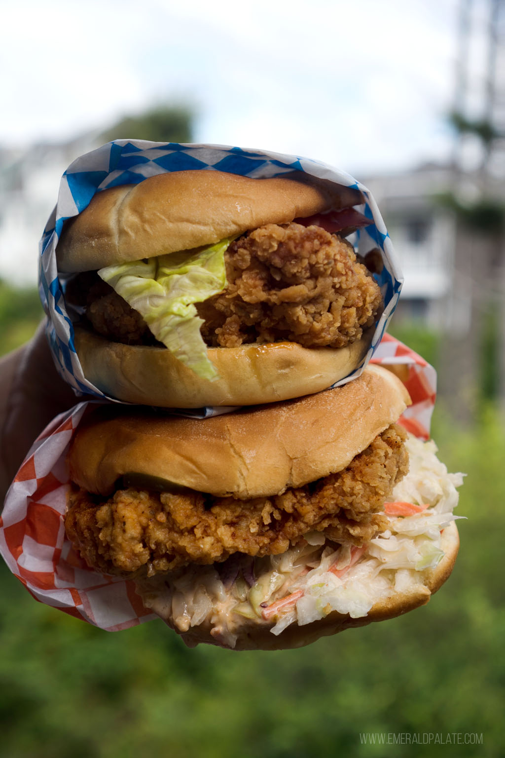 person holding two fried chicken sandwiches on top of each other