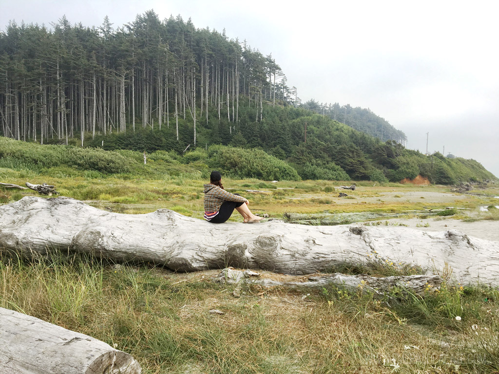 woman sitting on a log on the beach in Seabrook, a quaint WA beach town