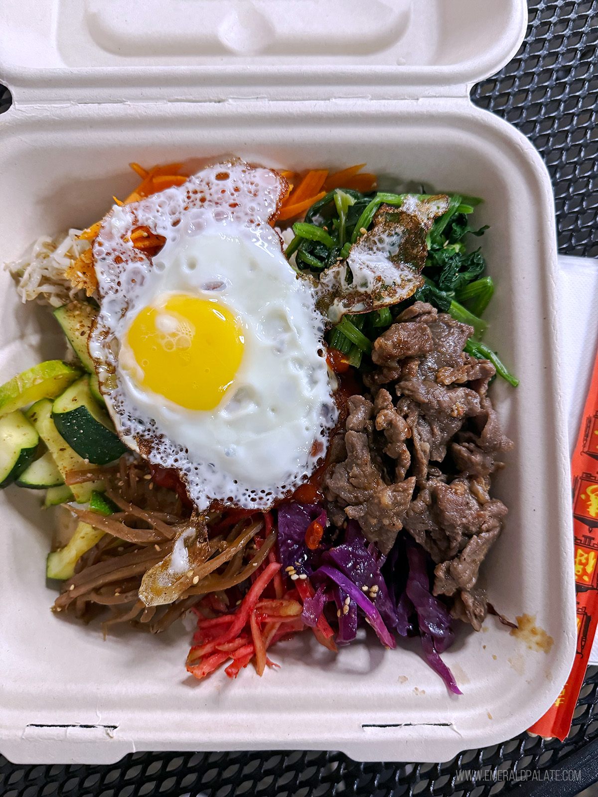 bibimbap with an egg on it in a takeout container