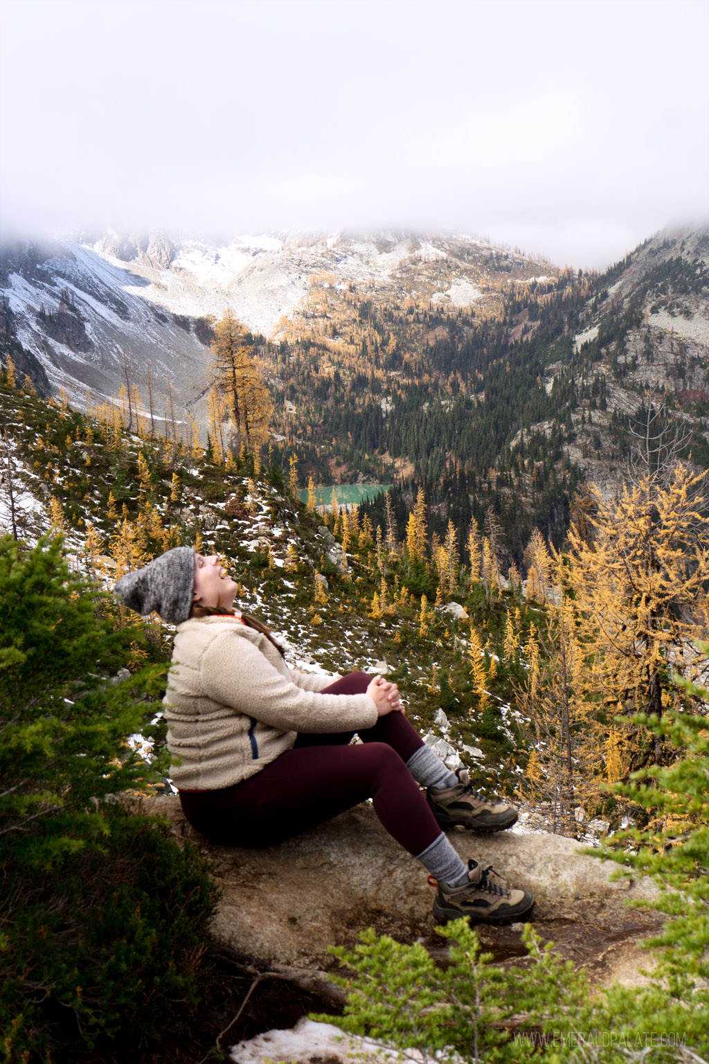 woman laughing on a ridge overlooking larches and mountains