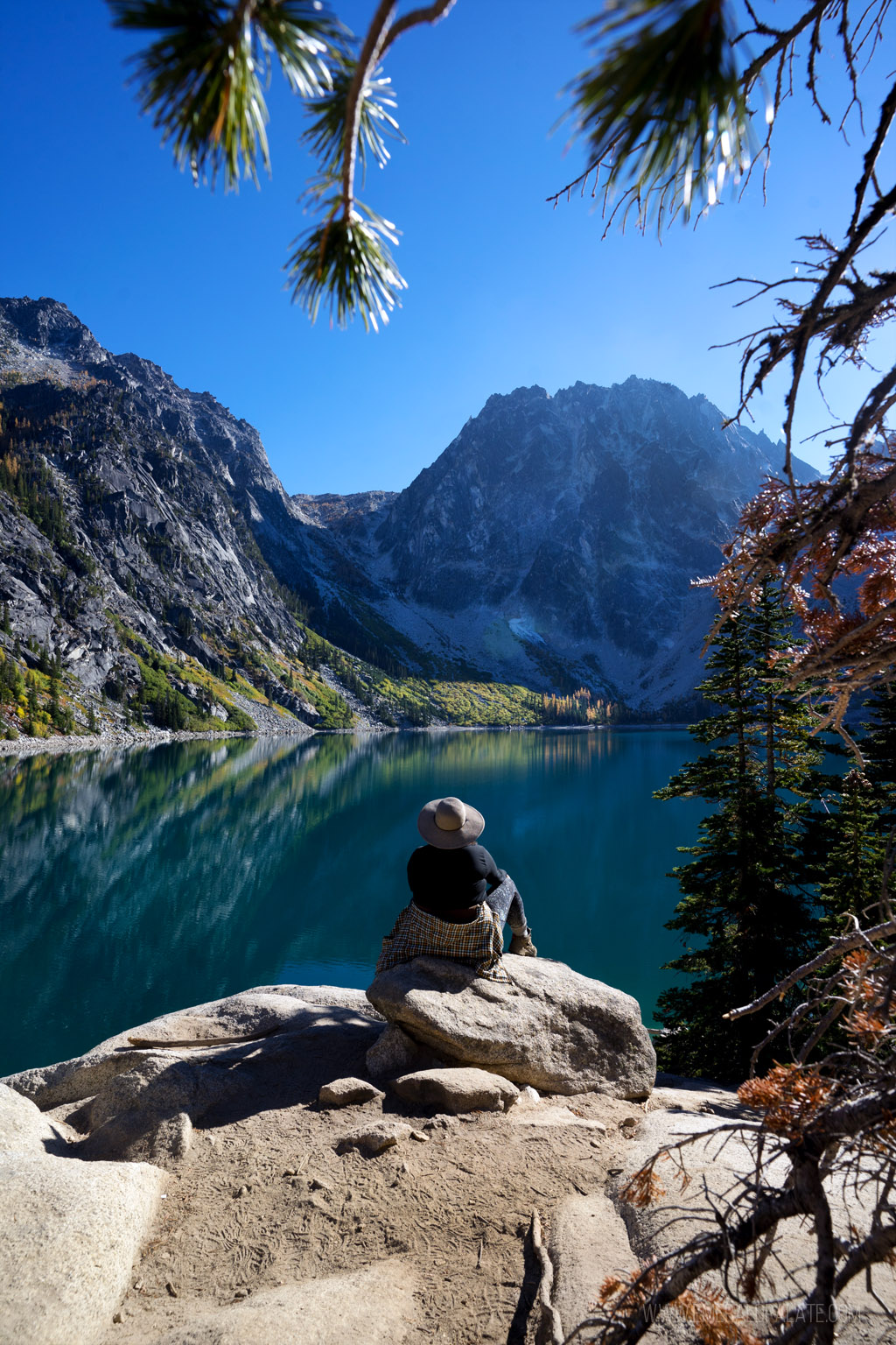 woman overlooking blue alpine lake surrounded by mountains on a larch hike in Washington state
