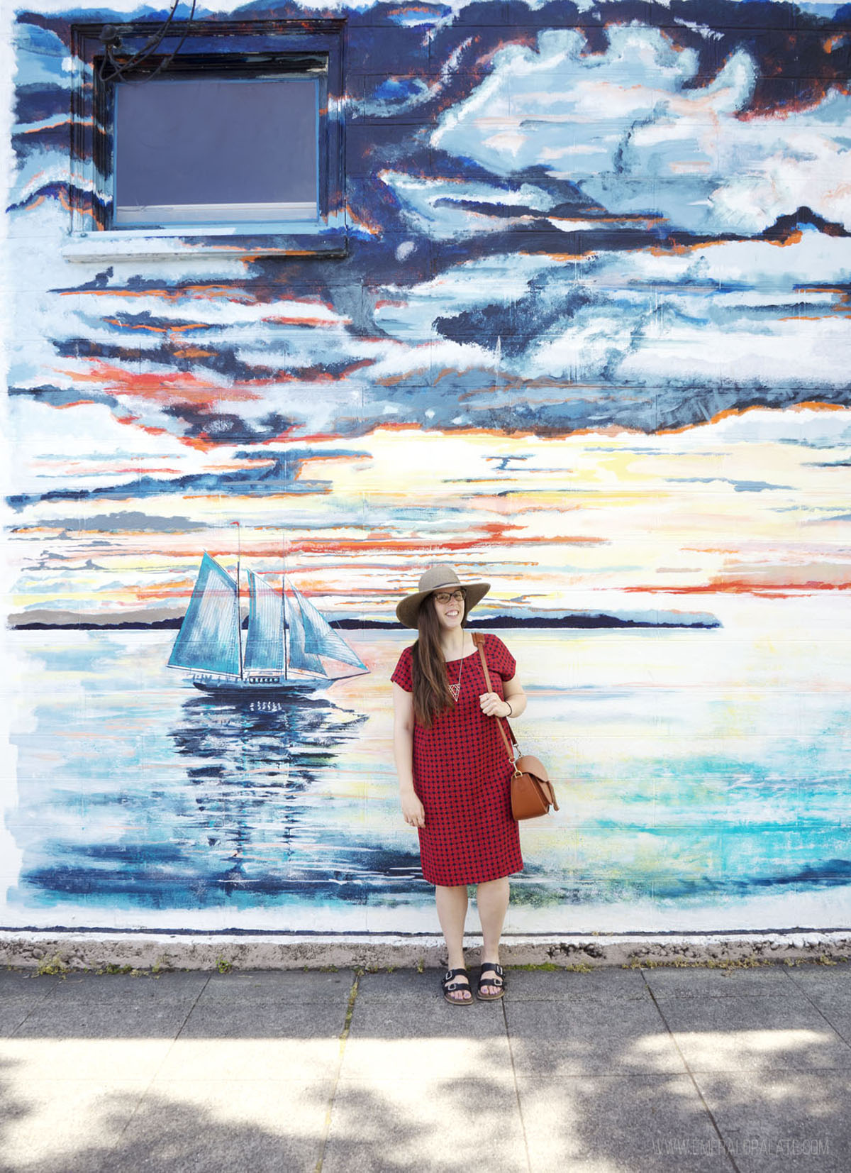 woman standing in front of an Edmonds mural of a sailboat on the water at sunset