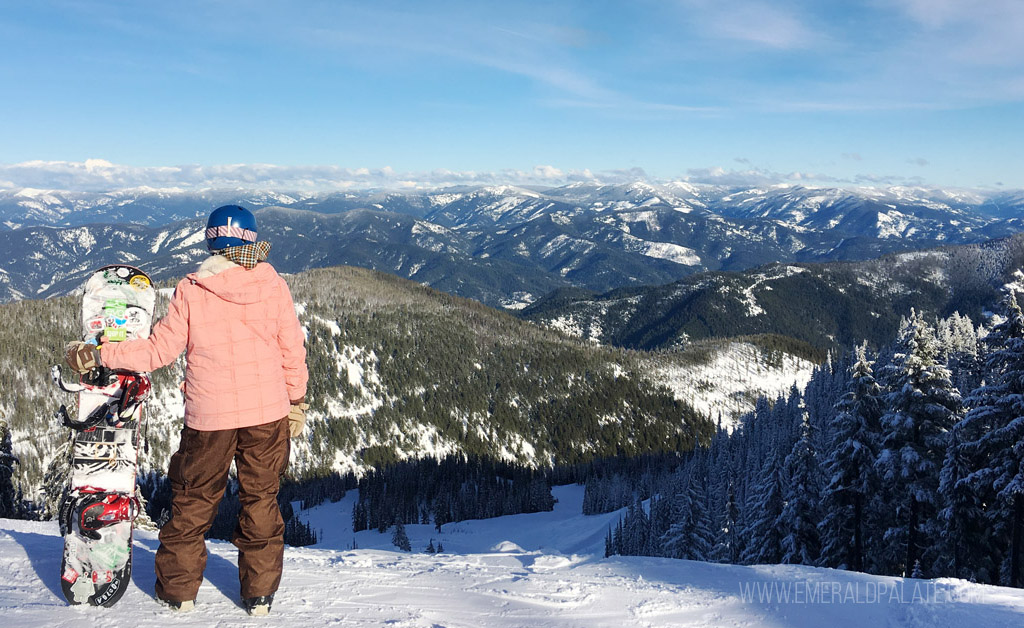 woman holding snowboard overlooking mountain scenery on sunny day