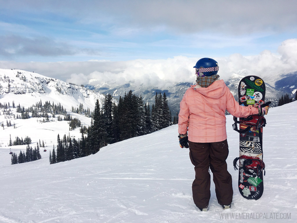woman holding snowboard overlooking ski resort