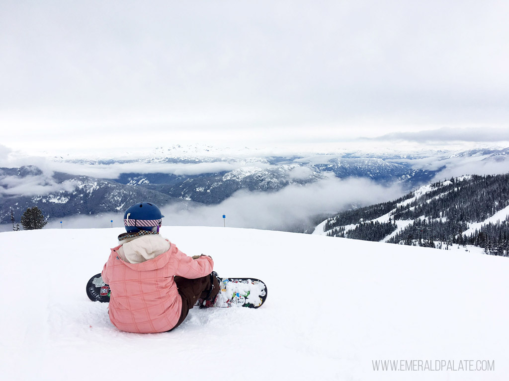 woman snowboarding sitting on mountain overlooking resort
