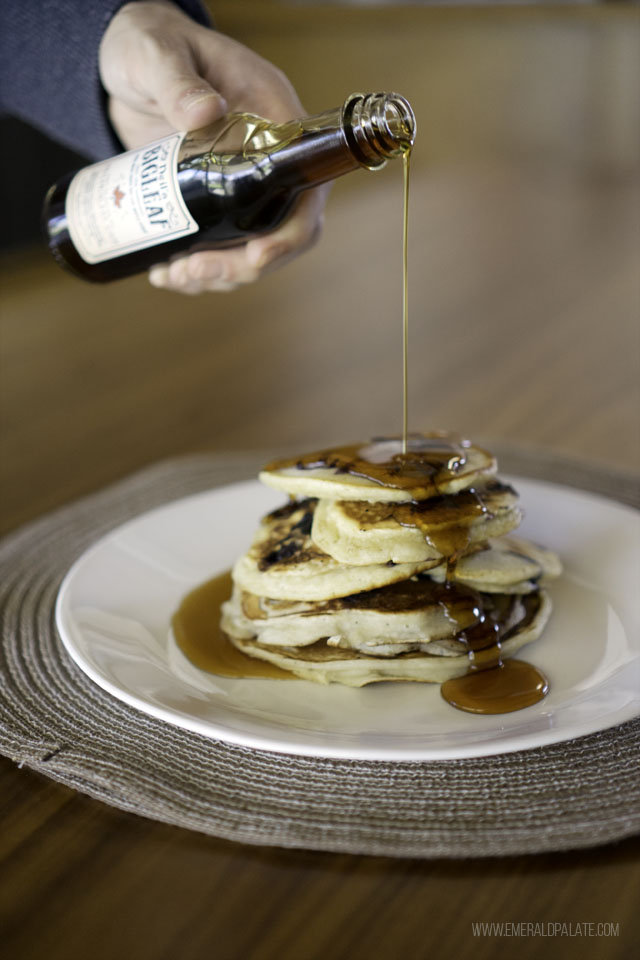 person pouring maple syrup over pancakes, both a must when stocking your pantry