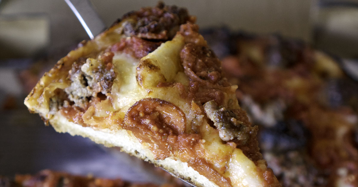 Close up of person holding up deep dish pizza with pepperoni, sausage and meatballs