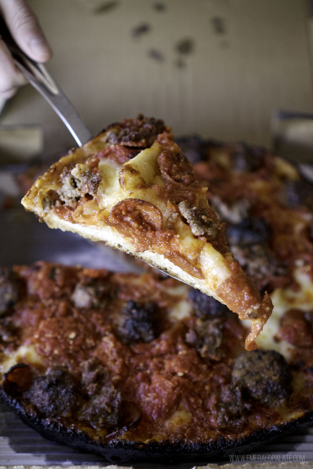 person taking slice of Detroit style pizza with meat on it from one of the best pizza places in Seattle