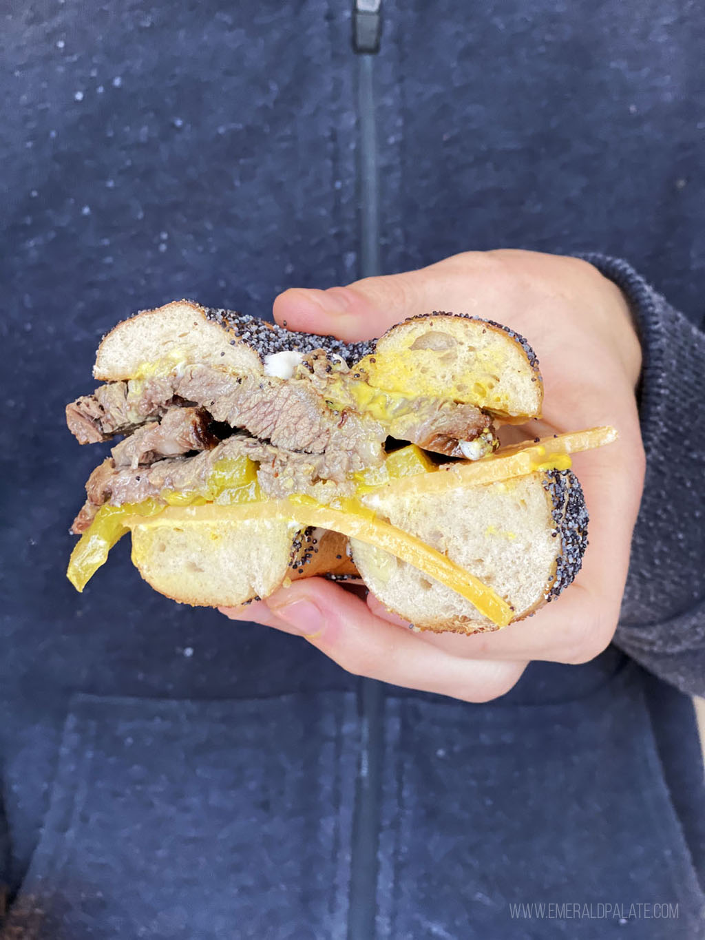 person holding half of a bagel sandwich with corned beef and cheese