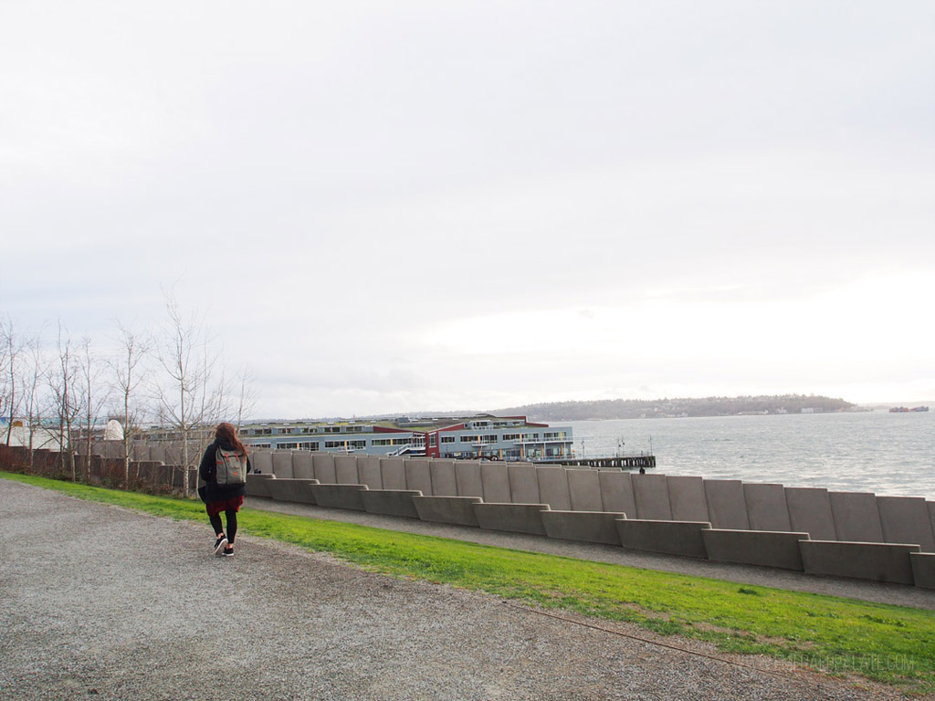 woman walking along trail with viewpoint of Seattle waterfront on Puget Sound