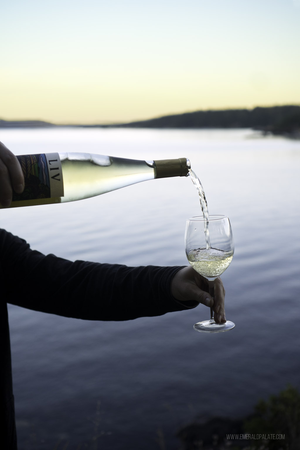 close up of man pouring white wine in a glass overlooking water at sunset on Lopez Island