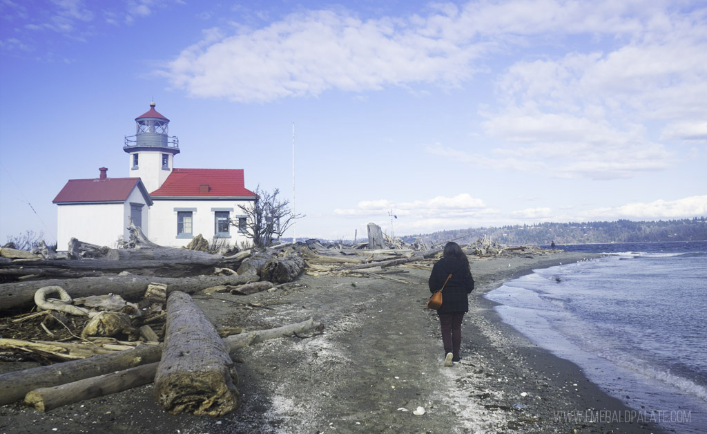 Woman walking on beach with lighthouse, a scenic day trip from Seattle