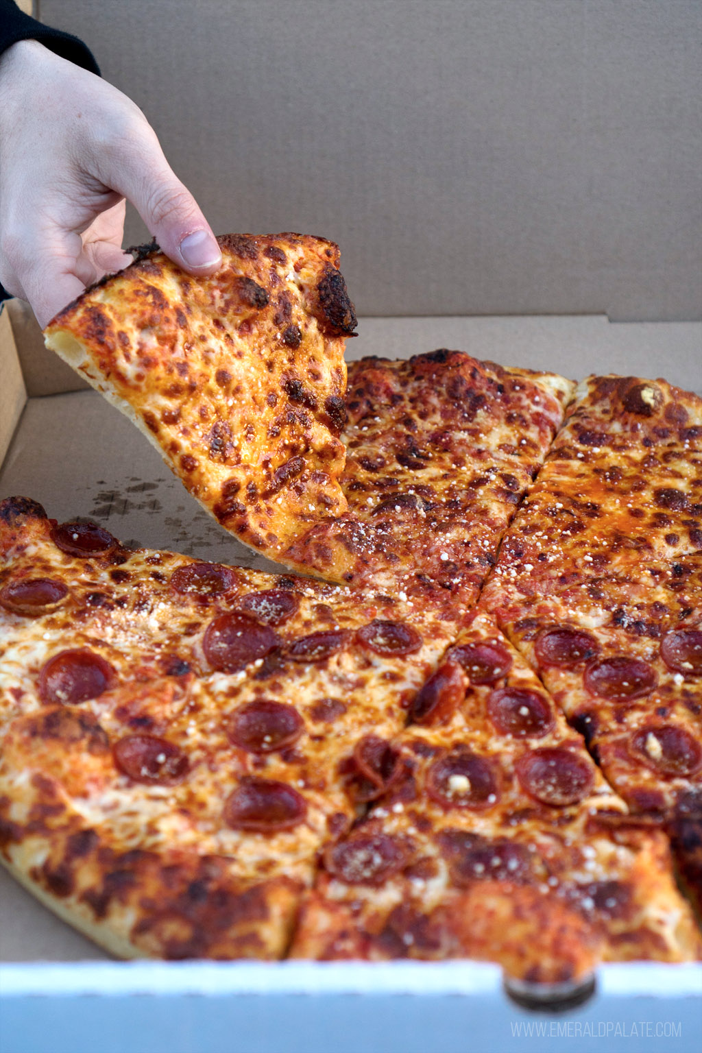 person picking up a slice of pizza from a pizza box