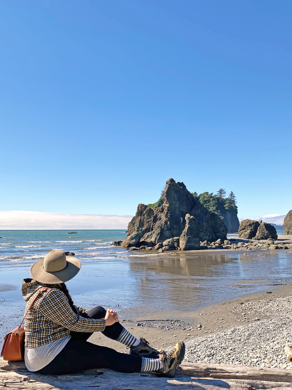 woman sitting on driftwood at Ruby beach, an attraction on the Washington coast