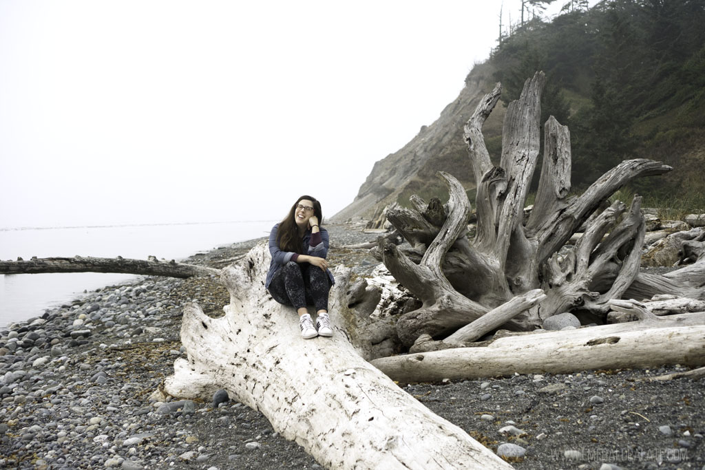 woman sitting on driftwood at Ebey State Park beach, one of the best things to do on Whidbey Island