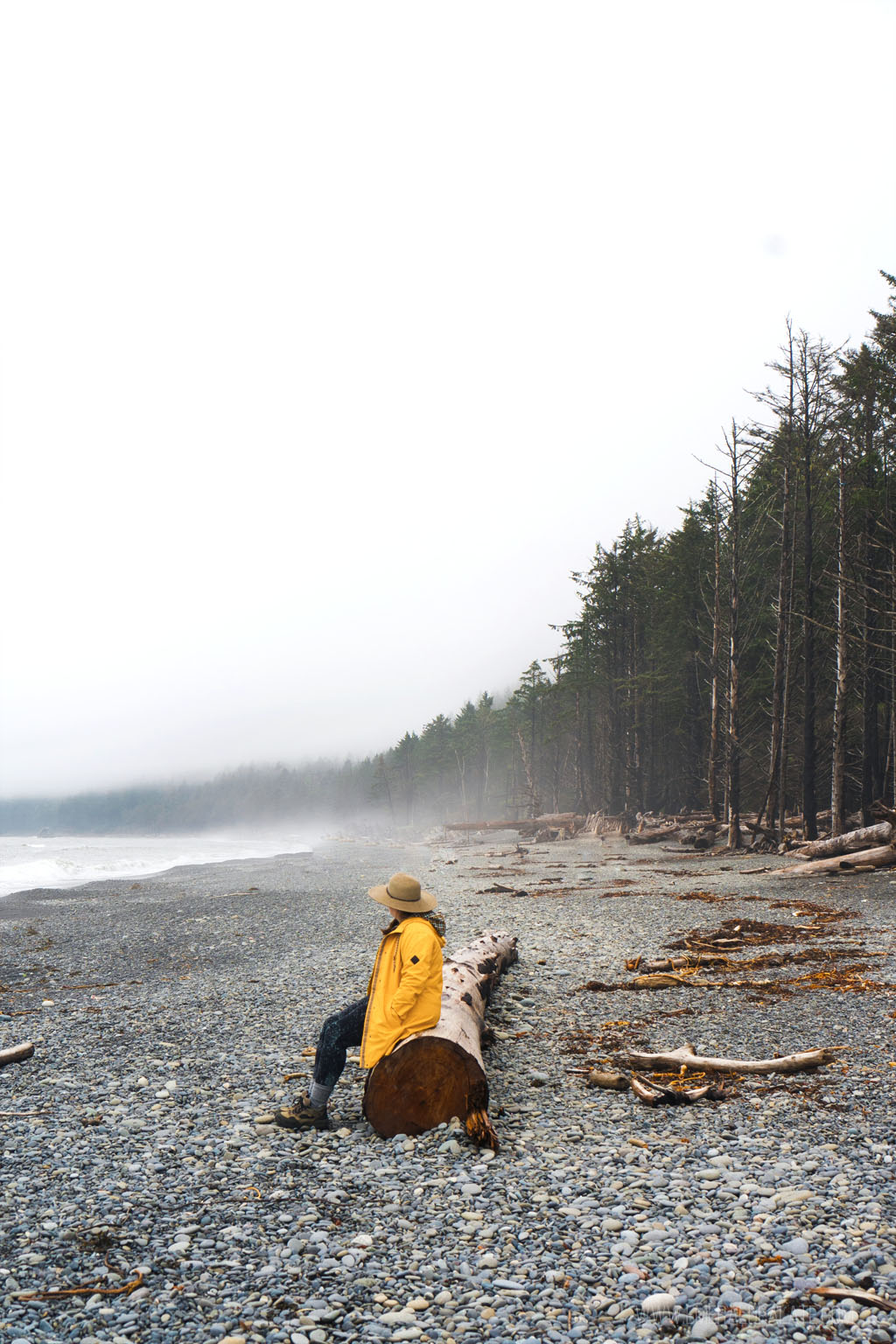 woman in rain coat sitting on log on Rialto Beach on misty day