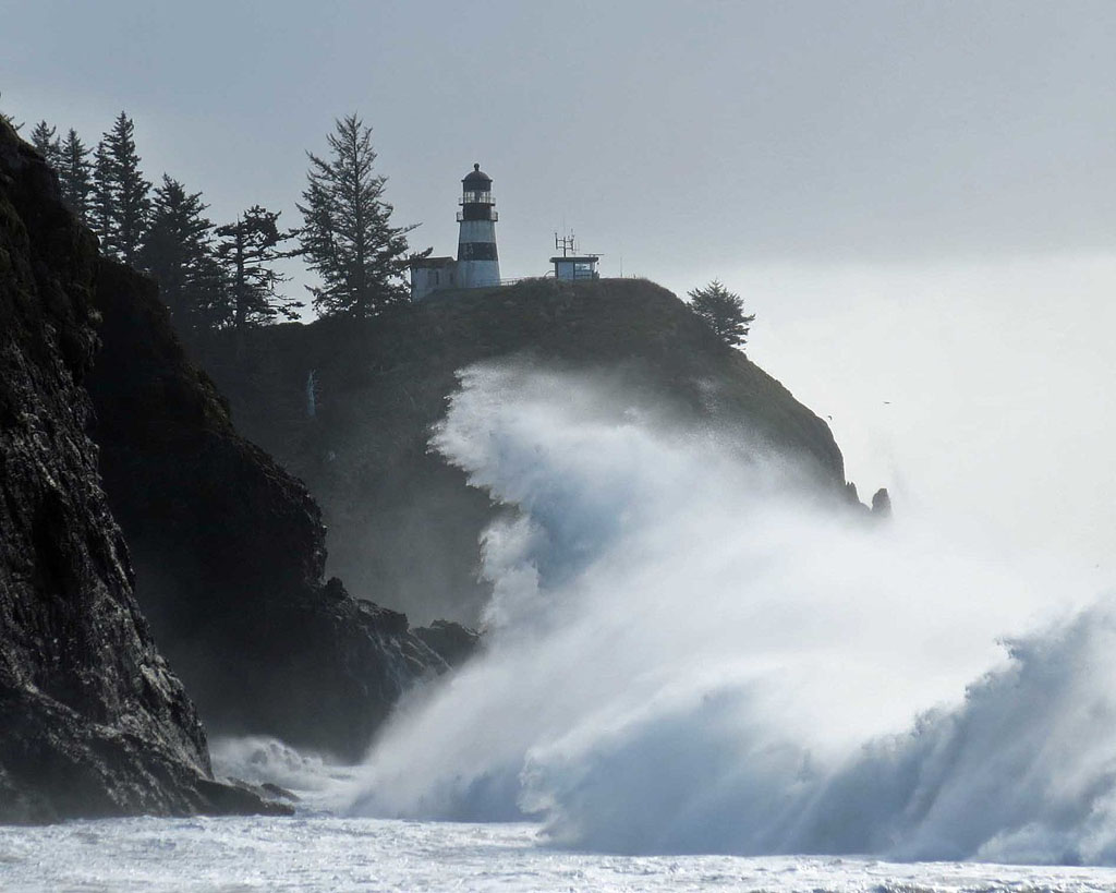 wave crashing on the cliffs with a lighthouse in the background at Cape Disappointment on the WA coast