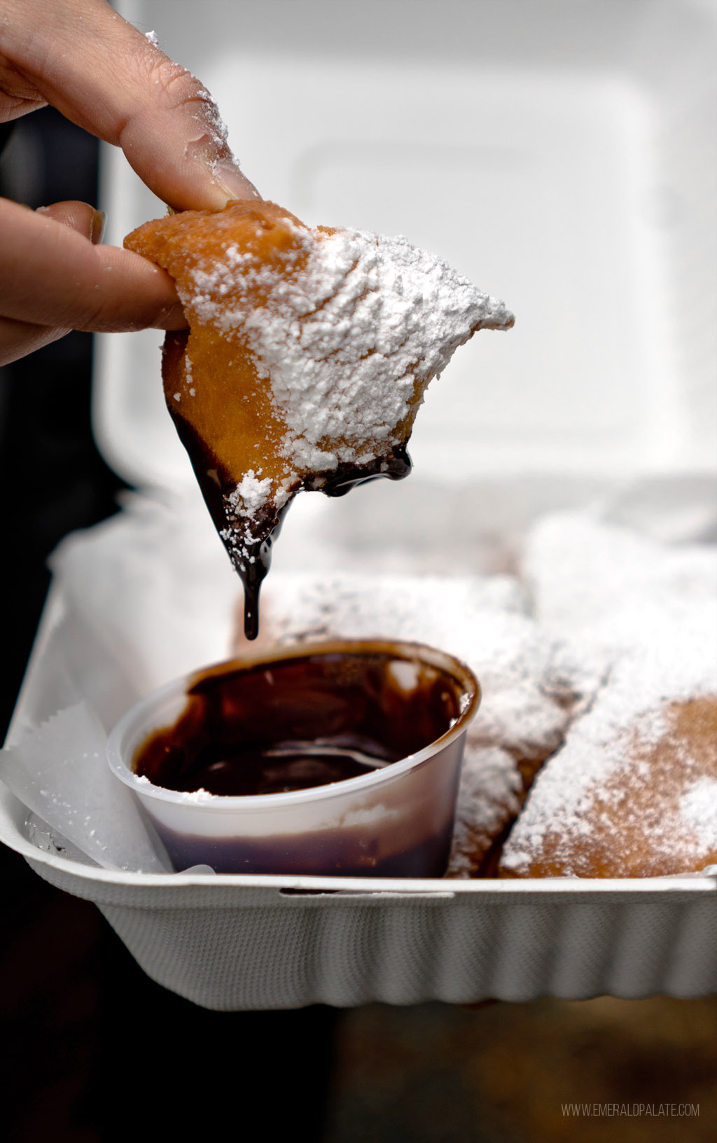 person dunking beignet into chocolate sauce