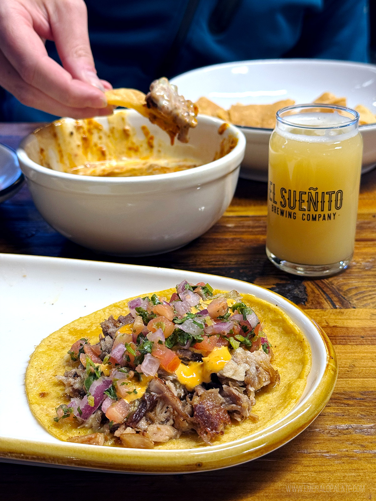 person dipping a chip in queso behind a carnitas taco