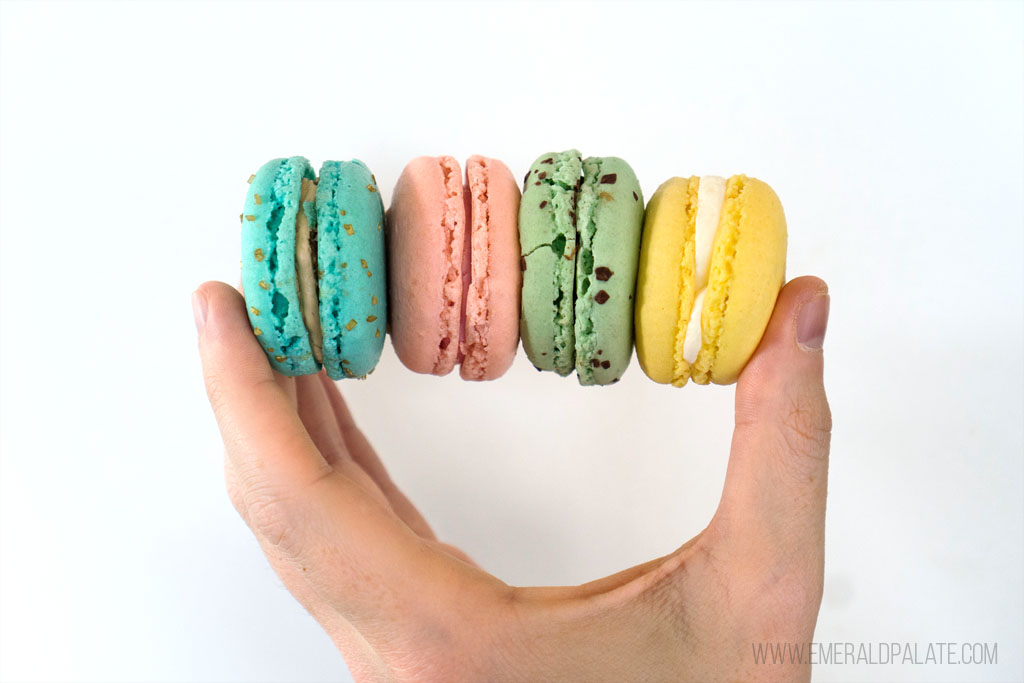 person holding 4 colorful macarons from one of the best Seattle dessert delivery