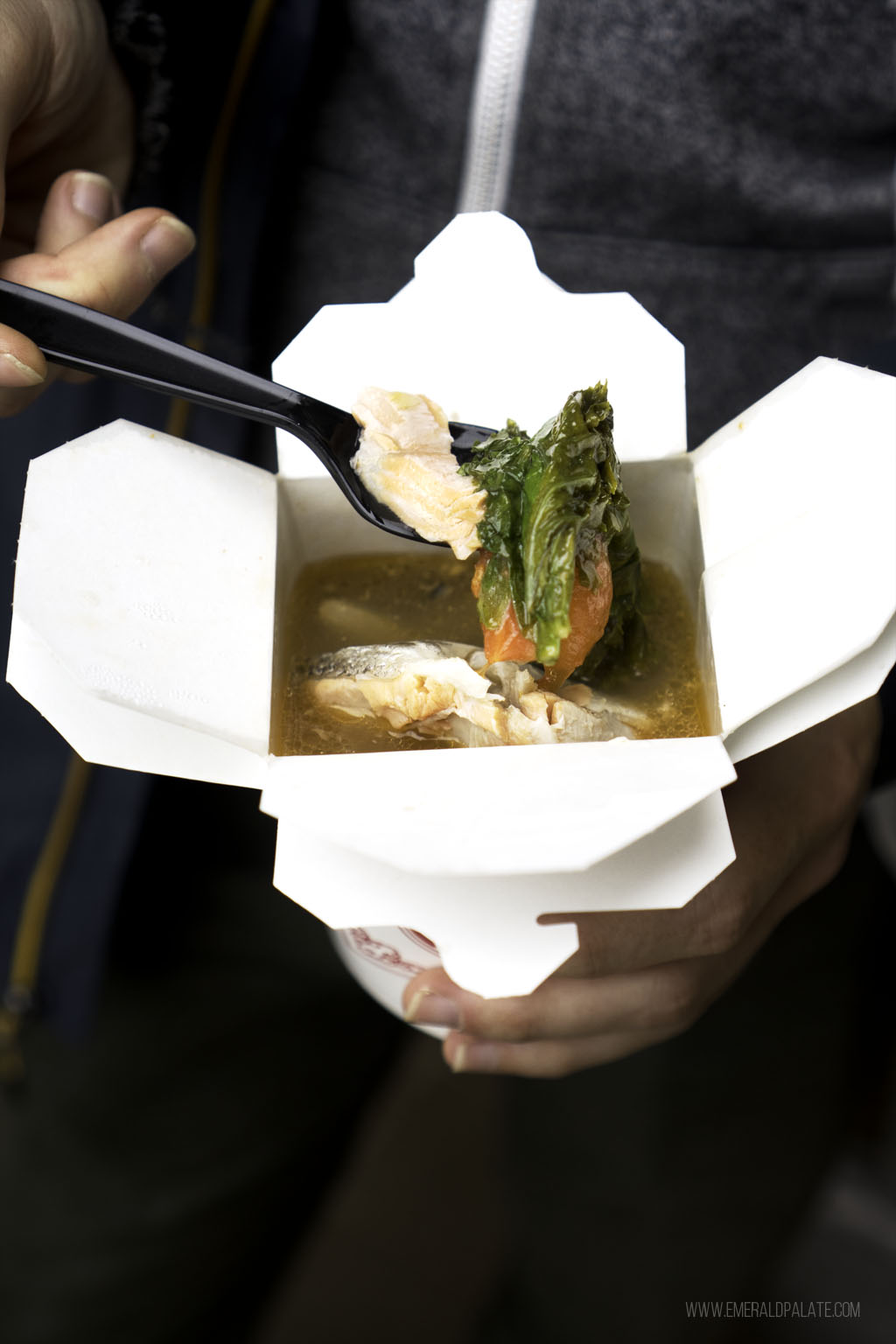 person taking a spoonful of salmon soup in Seattle out of a takeout container