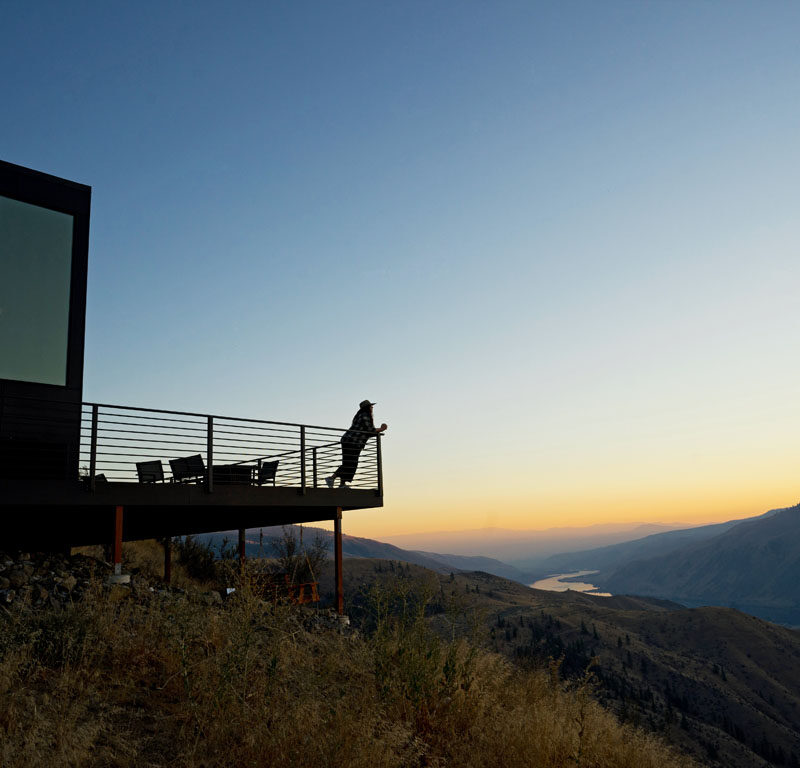 woman on balcony of a romantic Airbnb in Washington state overlooking a serene valley at sunset