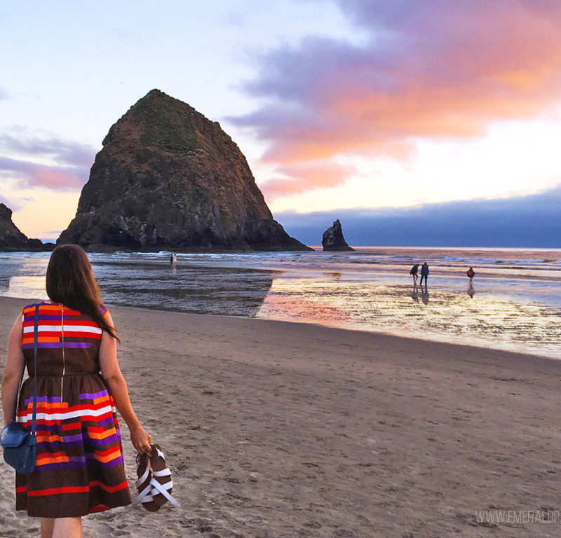woman looking out at haystack rock on Cannon Beach during sunset, one of the best road trips from Seattle