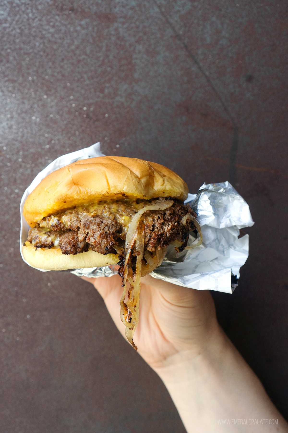 person holding a double patty smash burger with onions