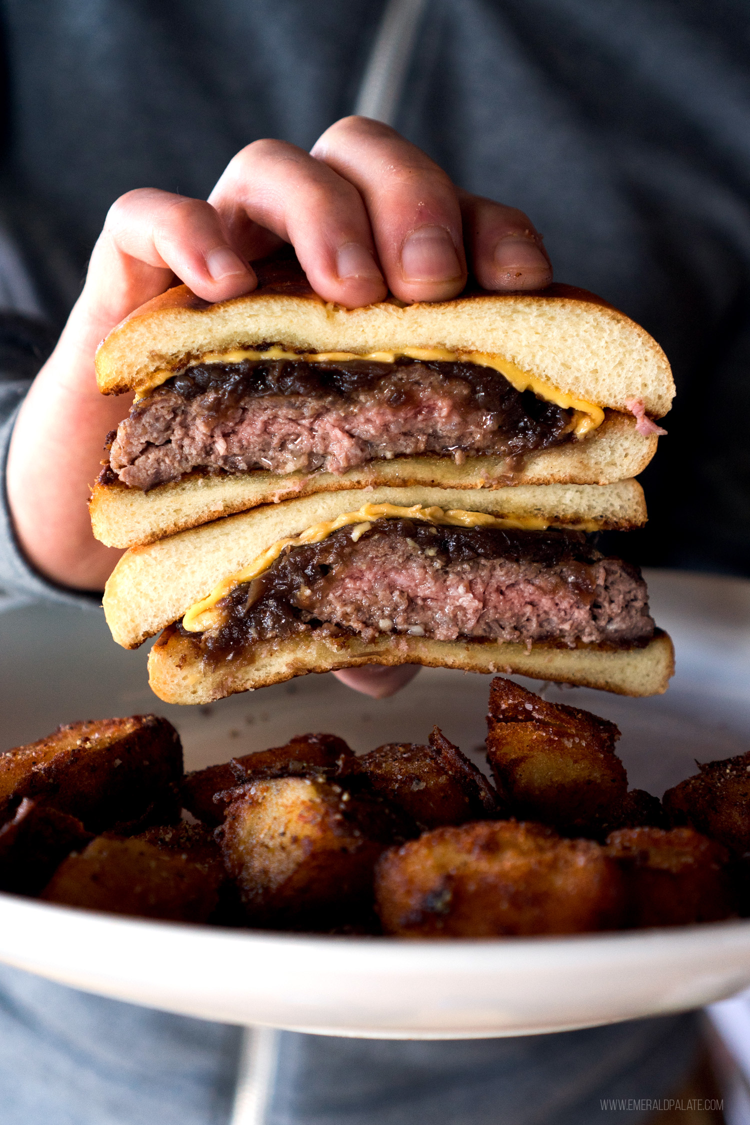 person holding drive-in style burger above potatoes