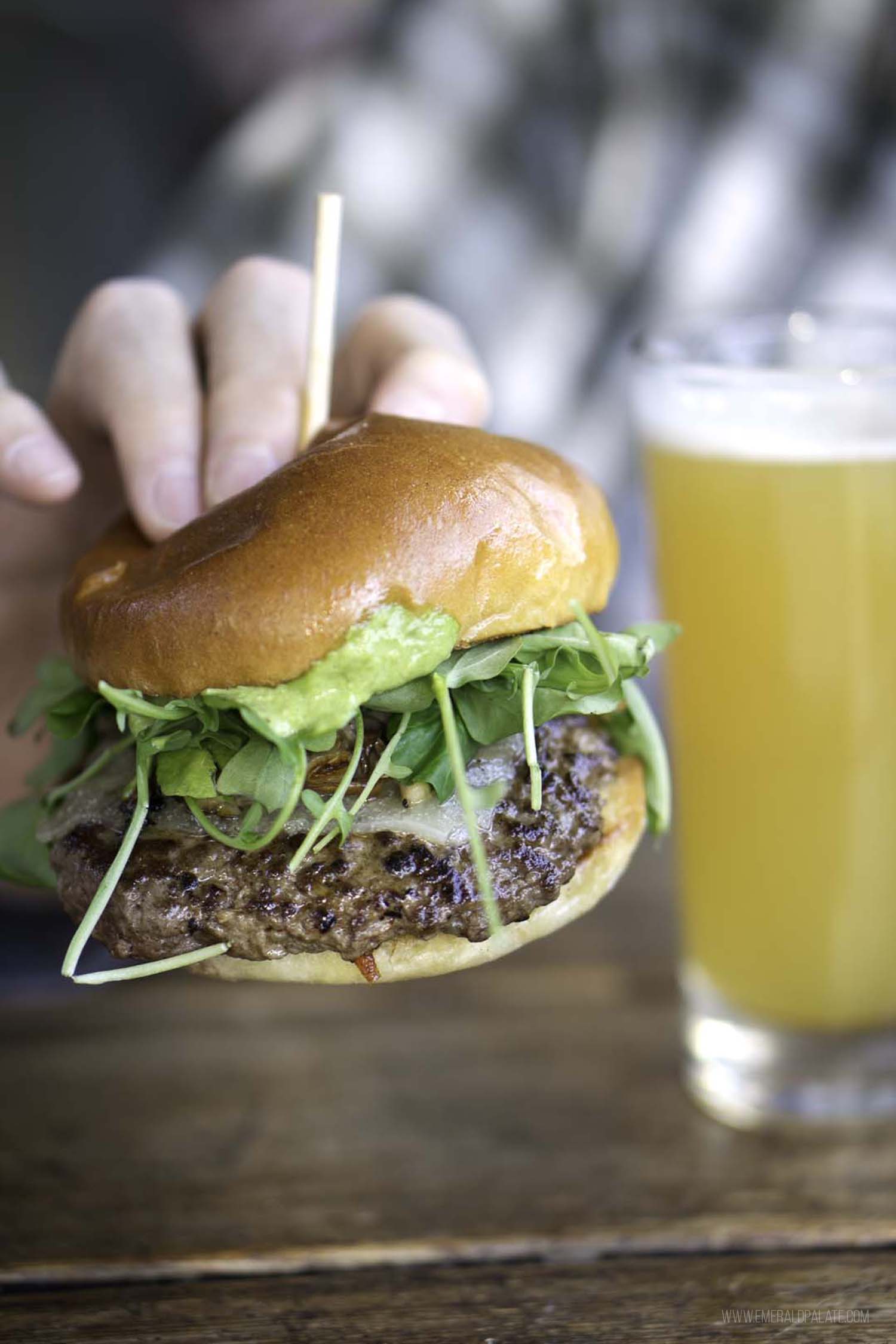 person holding burger with microgreens on it and beer
