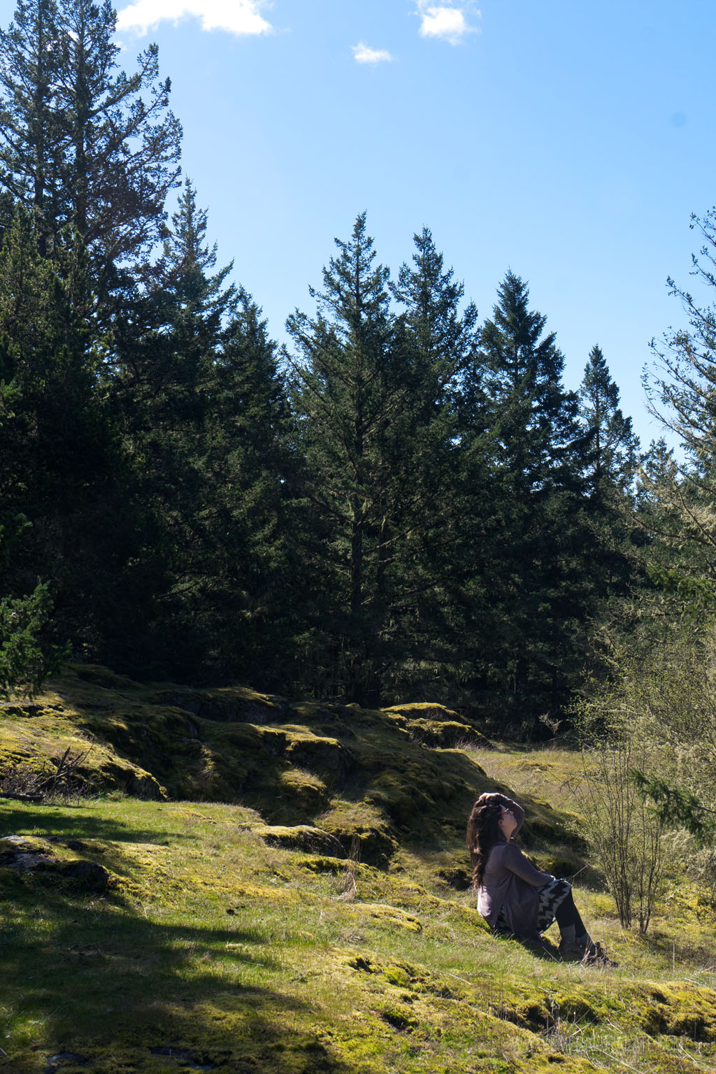 woman sitting on grassy knoll surrounded by trees on Lopez Hill