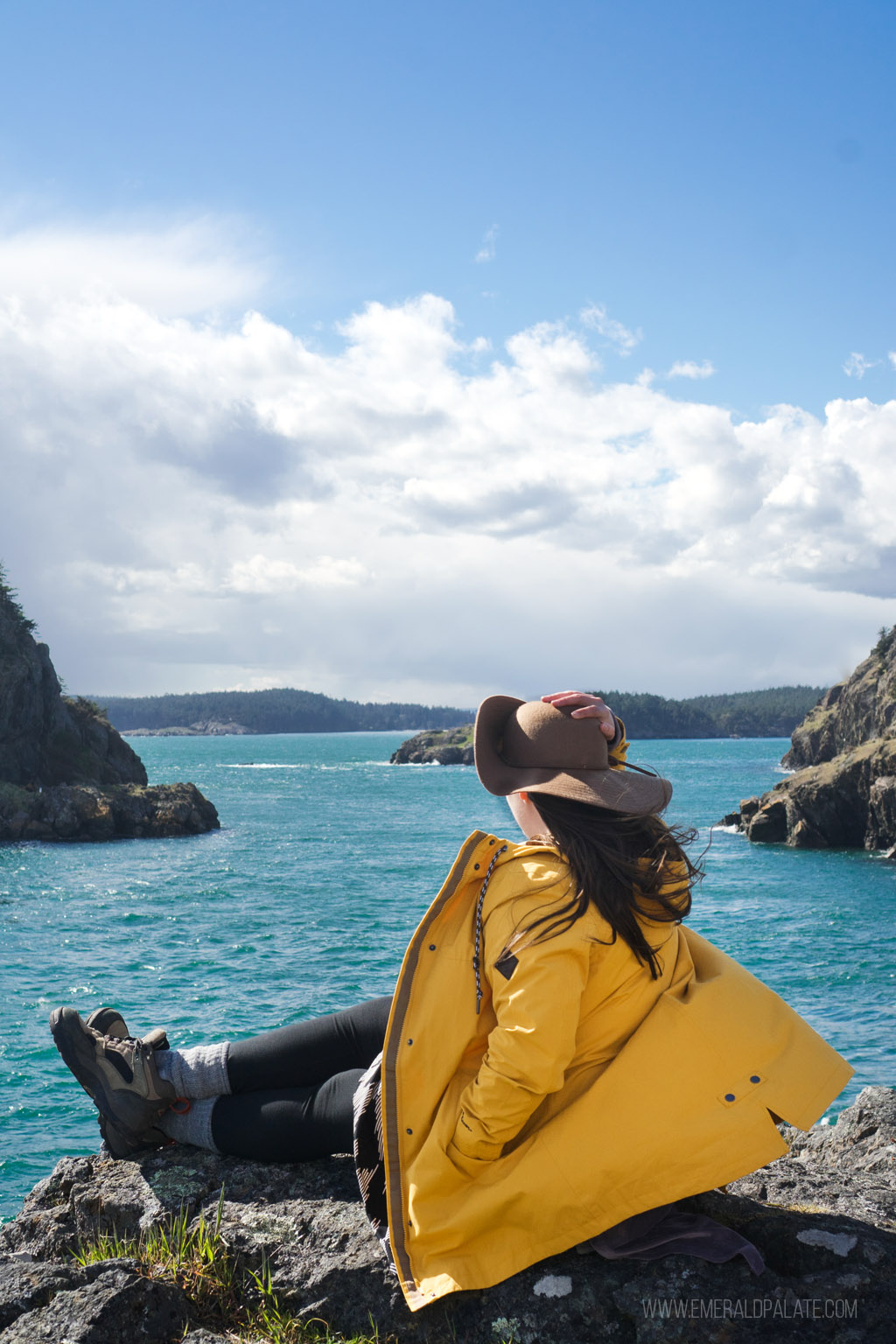 woman holding hat in wind on cliff at Point Colville, one of the best things to do on Lopez Island