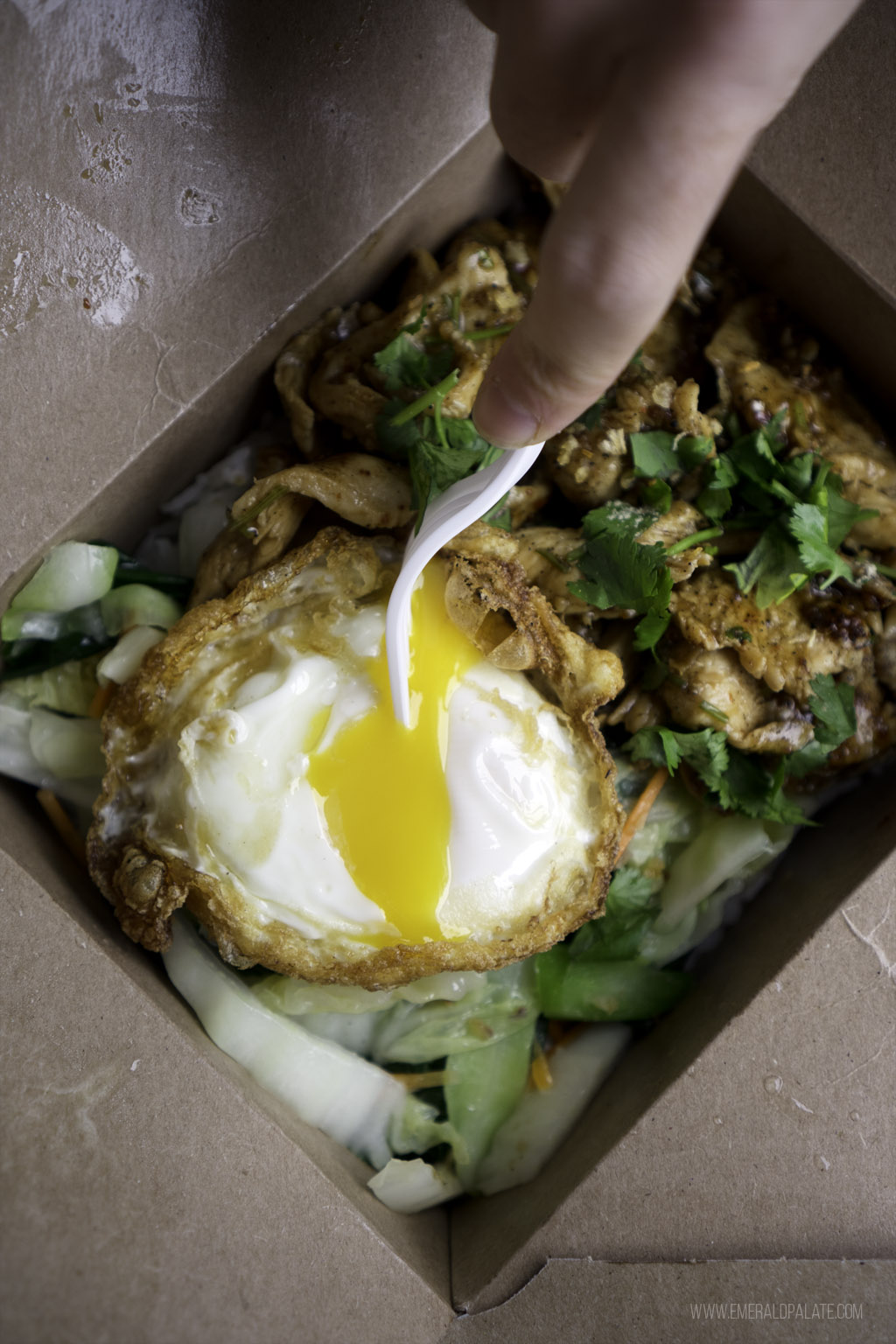 person breaking egg yolk in a noodle dish from a Thai restaurant