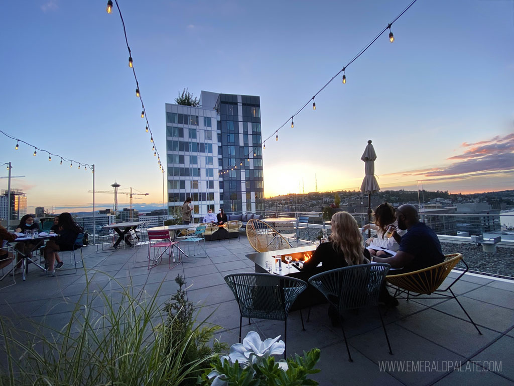 People eating and drinking on a Seattle rooftop bar with Space Needle in the distance