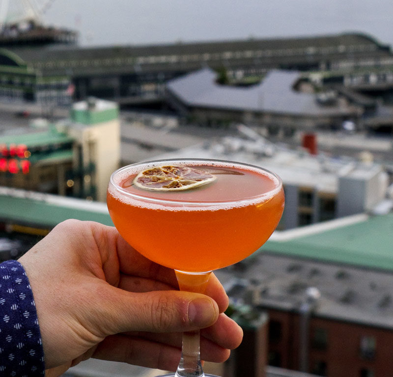 person holding cocktail above view of city skyline off one of the best rooftop bars in Seattle