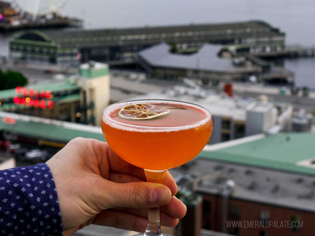 person holding cocktail in front of downtown Seattle at one of the best rooftop bars in Seattle