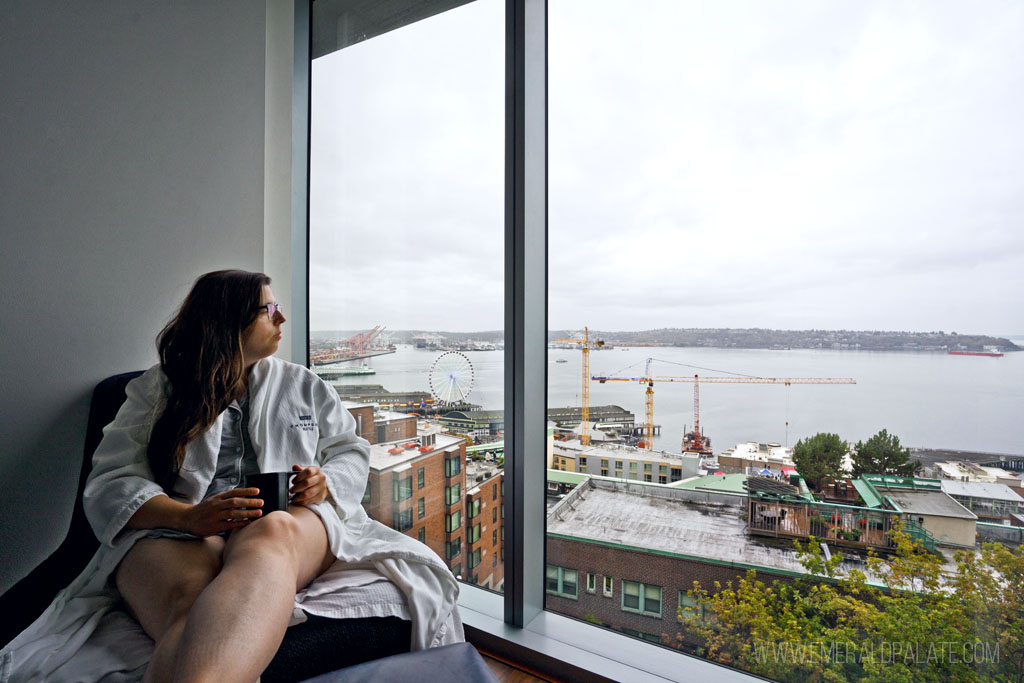 woman sitting on lounge chair in robe enjoying coffee and view of Seattle from a hotel room